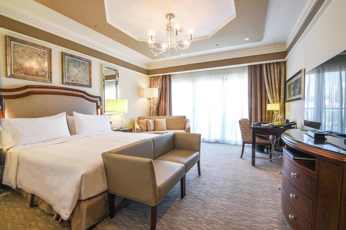 A hotel room with a large bed, a sofa, a desk, and a television.