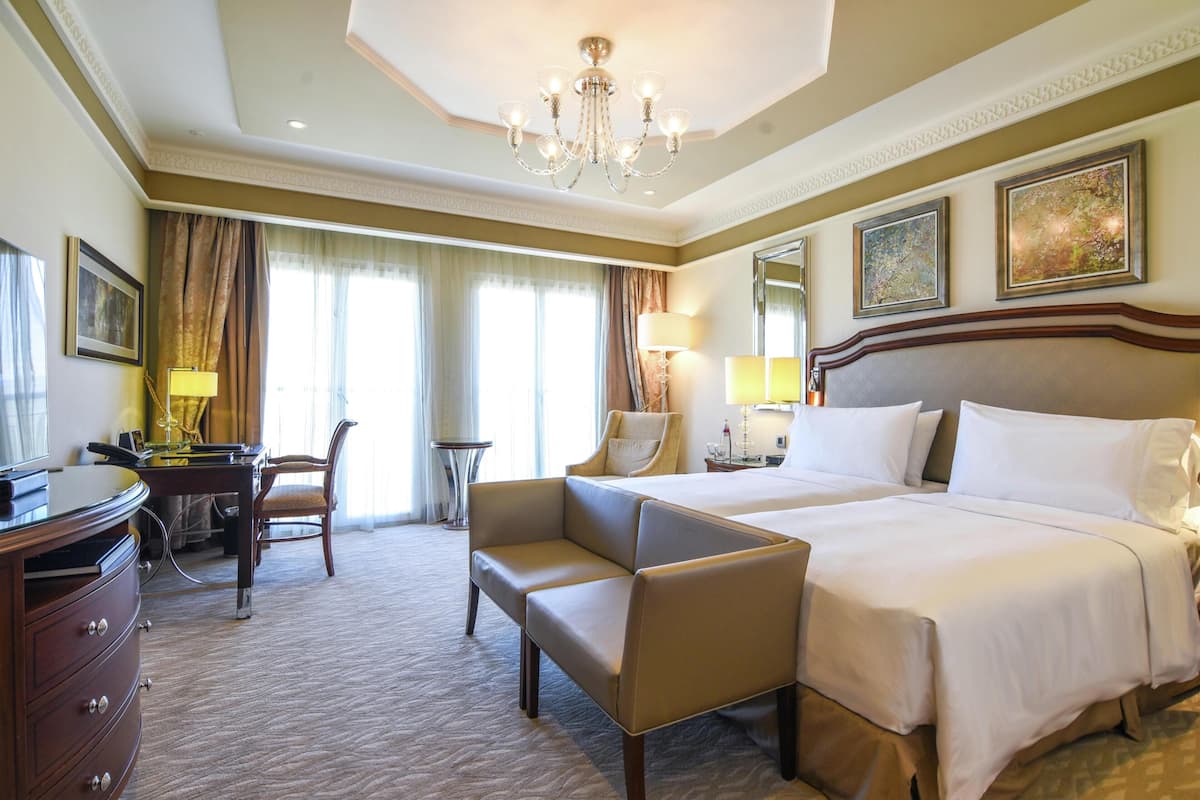 A hotel room with a large bed, a desk, a chair, and a chandelier.