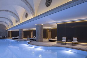 Una piscina interior moderna con sillones de descanso y una estructura de columna de piedra.