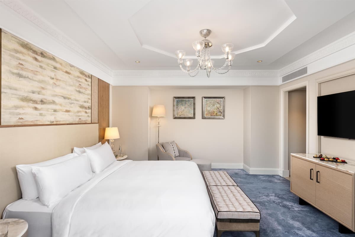 A hotel room with a large bed, a desk, a chair, a TV, and artwork on the walls.
