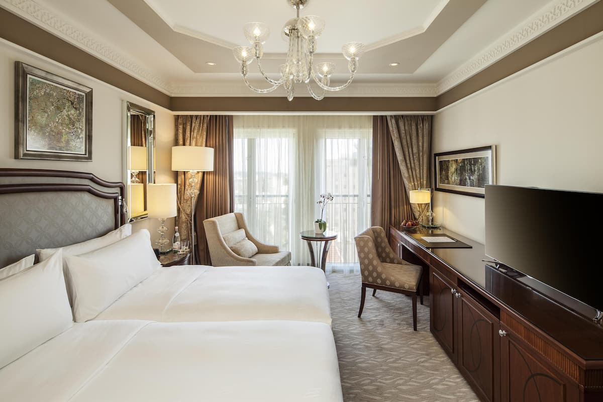 A hotel room with a large bed, a TV, a desk, and a chandelier.