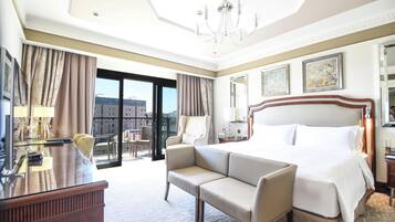 Habitación de hotel con cama, sofá, escritorio, silla, candelabro y vistas a edificios.