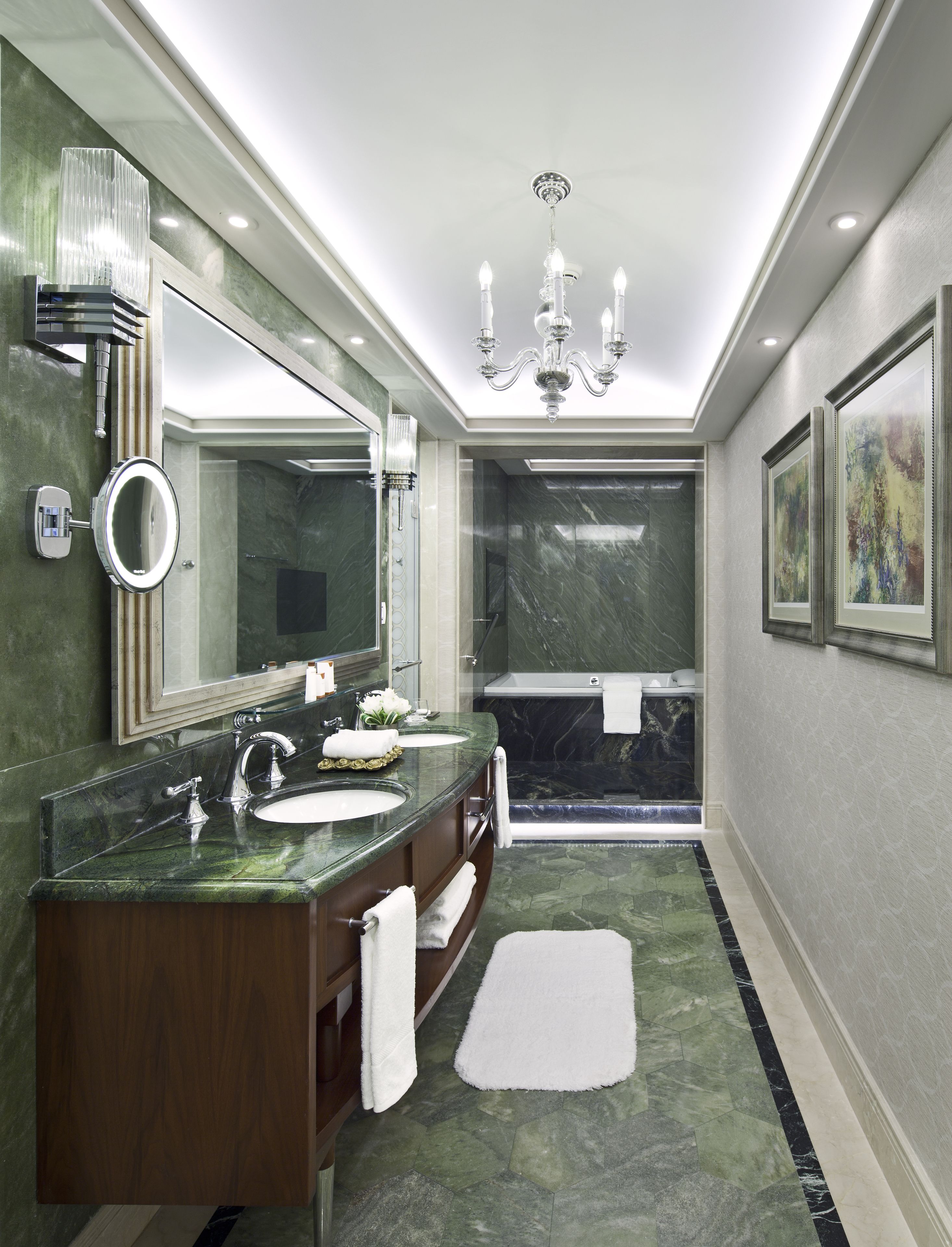 Une salle de bain moderne avec deux vasques, un grand miroir, un lustre et un sol en marbre.