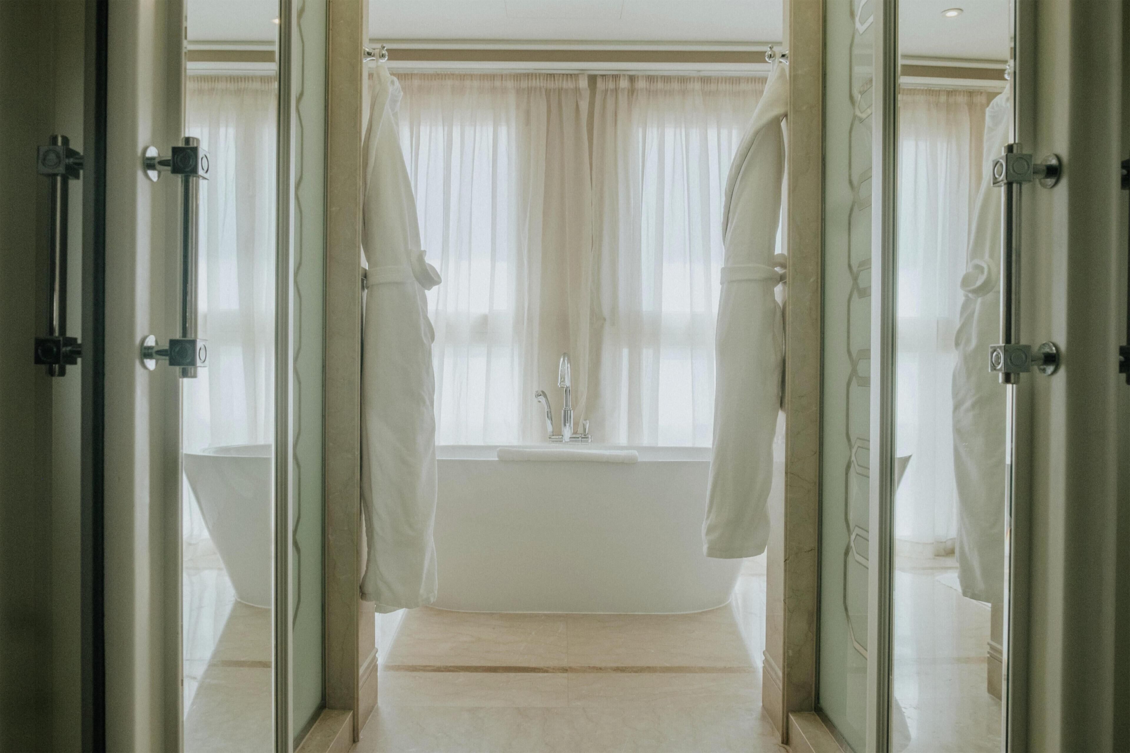 A bathroom with a bathtub, a sink, and a window with curtains.