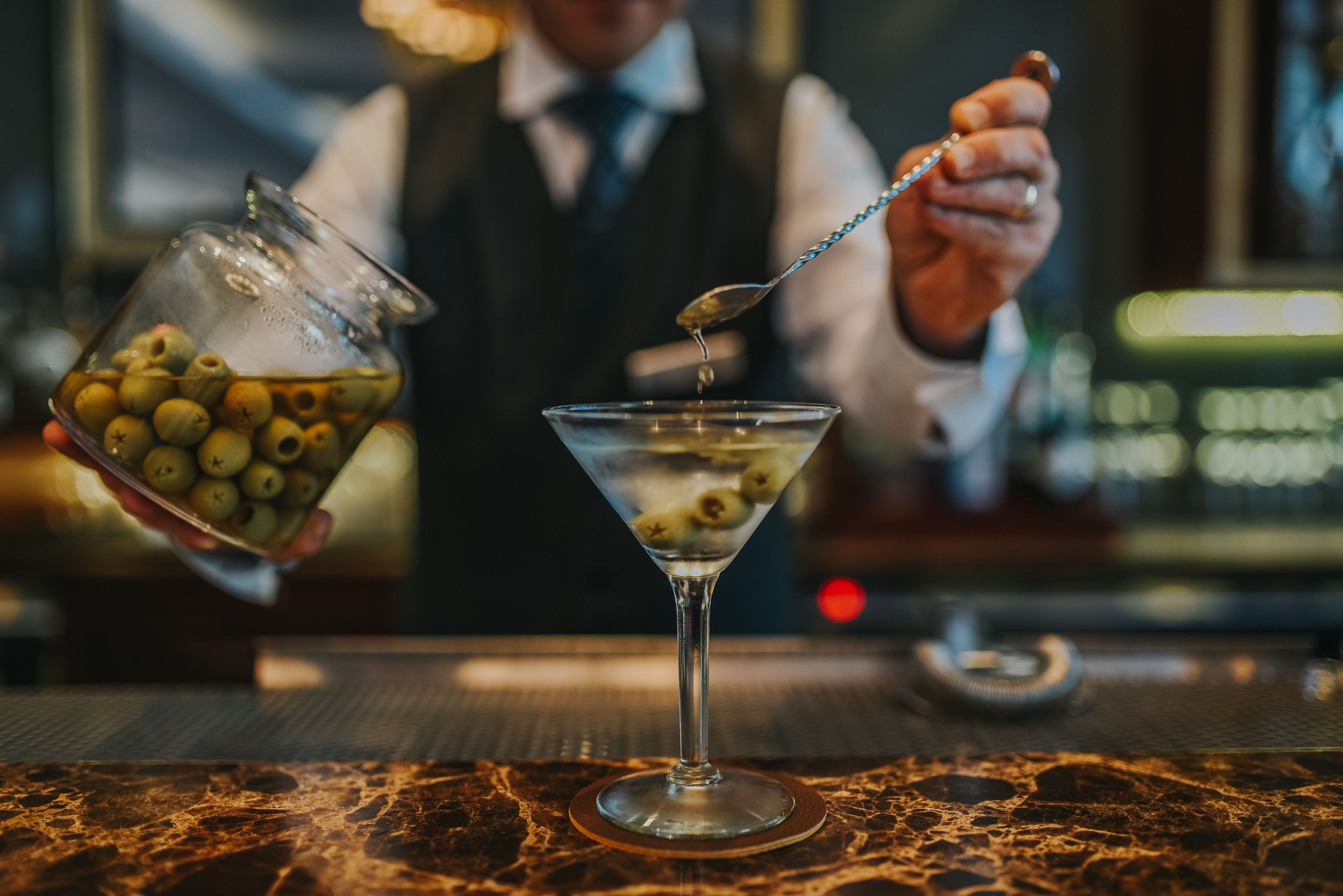 A bartender pouring a drink into a martini glass.