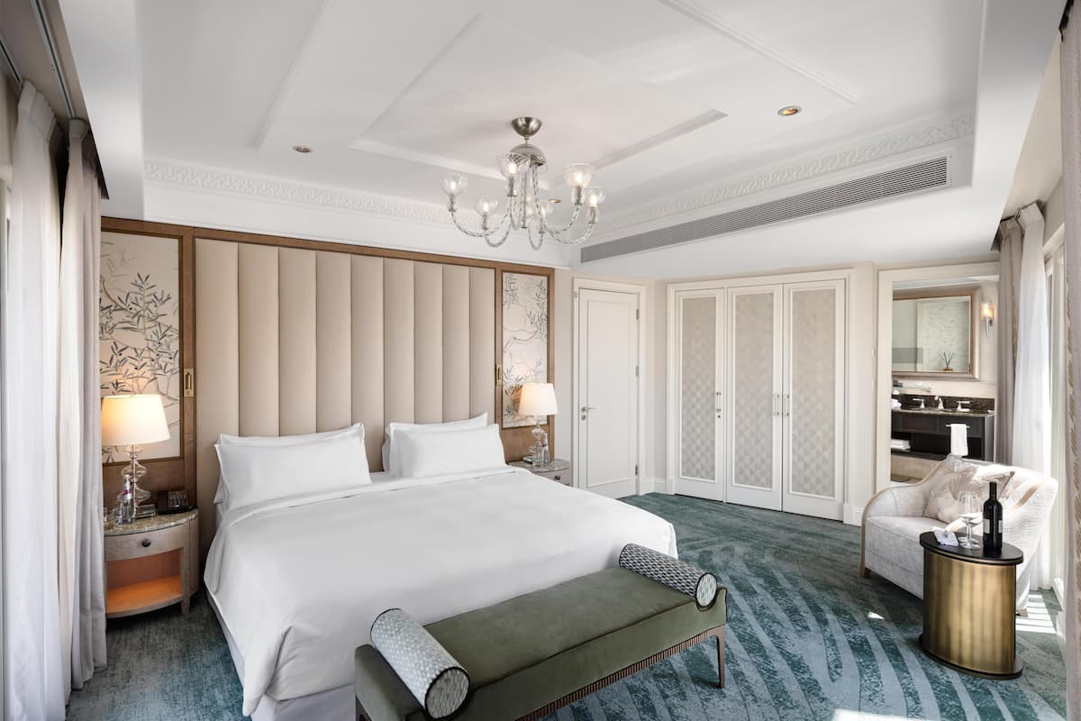 A hotel room with a large bed, a chandelier, a sofa, a side table, and a mirror.
