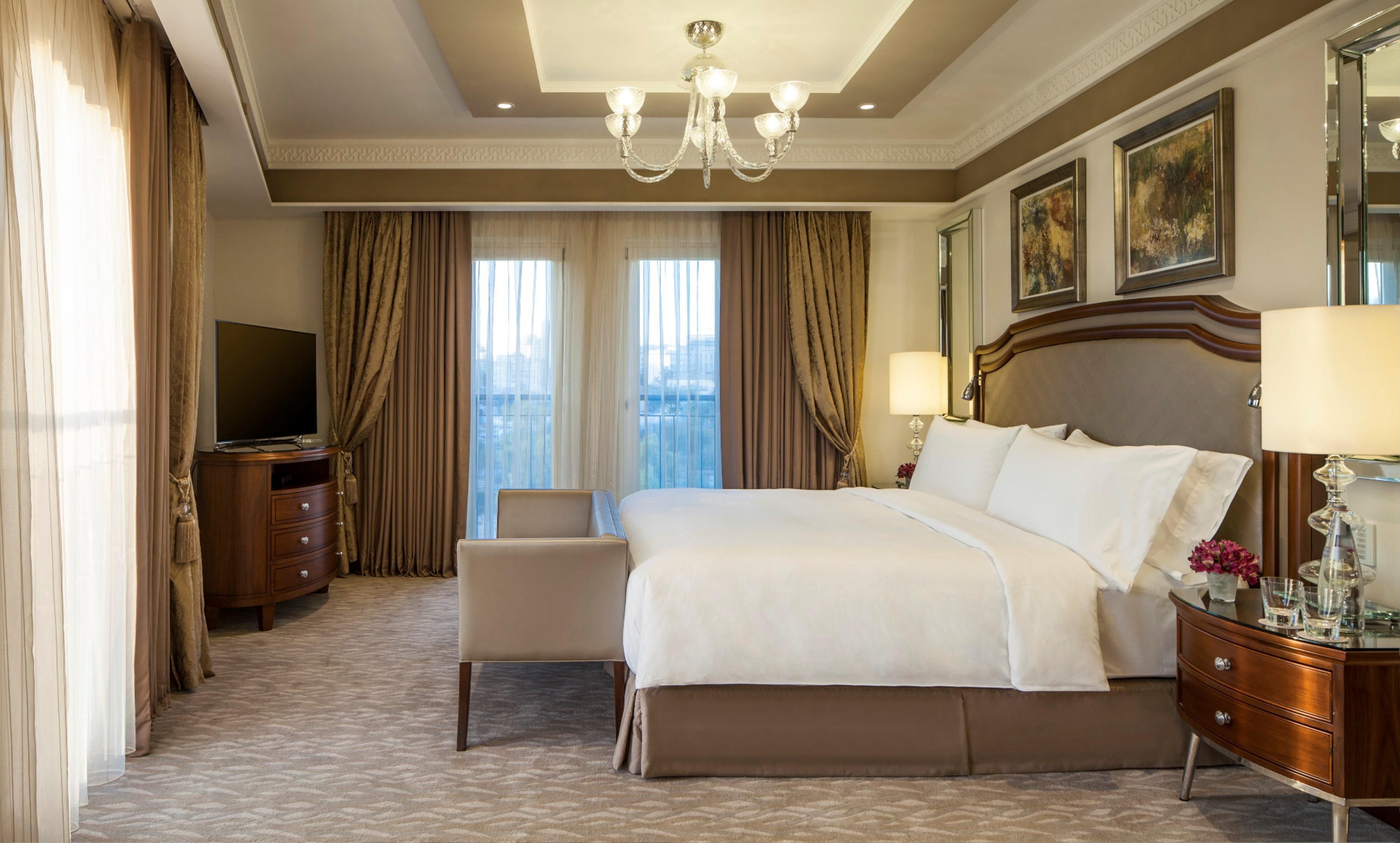 A hotel room with a large bed, a television, a desk, and a view of the city.