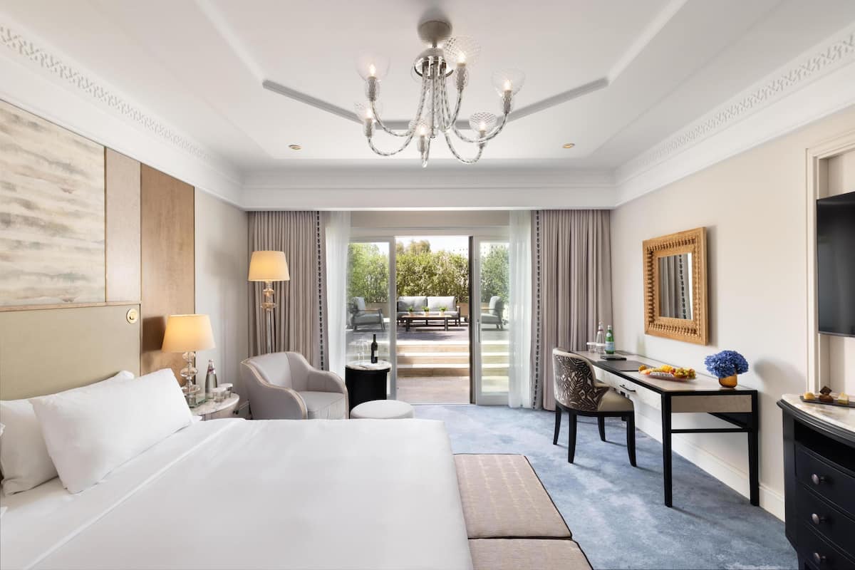 A hotel room with a large bed, a desk, a chair, a TV, and a view of the outdoors.