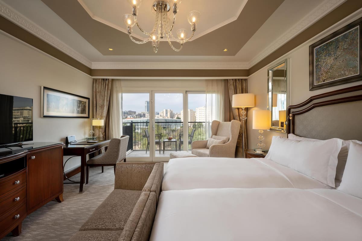 A hotel room with a large bed, a desk, a chair, a television, and a balcony with a city view.
