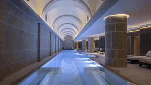 A long, narrow indoor swimming pool with stone columns and seating areas. - Waldorf Astoria Jerusalem (Jerusalem)