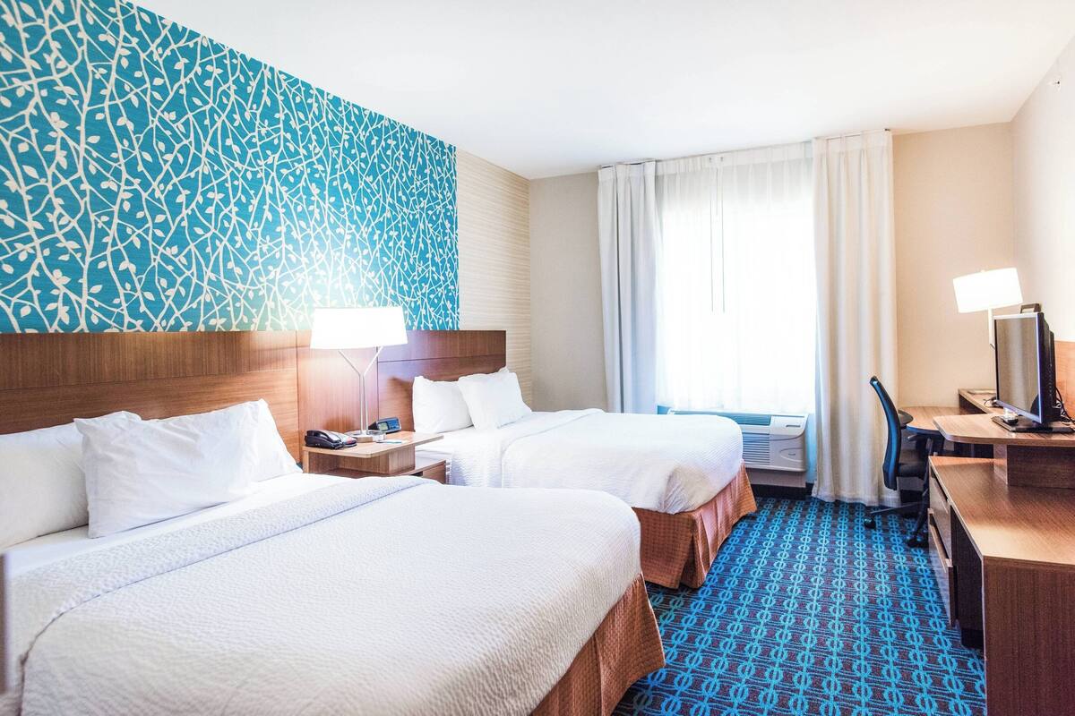 A hotel room with two beds, a desk with a computer, a TV, and a patterned carpet.