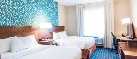 Habitación de hotel con dos camas, un escritorio con computadora, un televisor y una alfombra estampada.