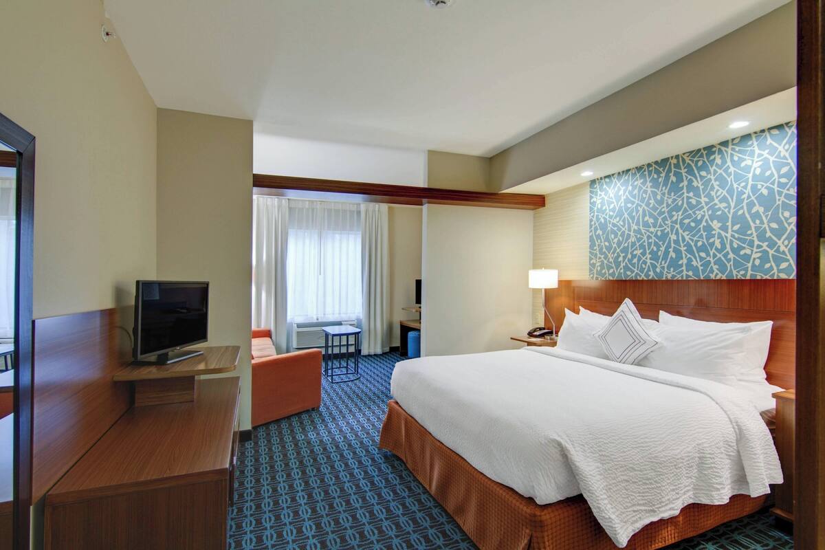 A hotel room with a bed, a TV on a stand, a desk, and a chair.