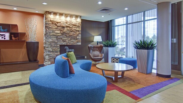 A modern lobby with a stone wall, blue seating, a round table, and large windows. - Fairfield Inn & Suites Natchitoches (Natchitoches)