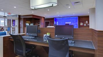A modern reception desk with two computer monitors, a large blue screen, and a wooden reception area.