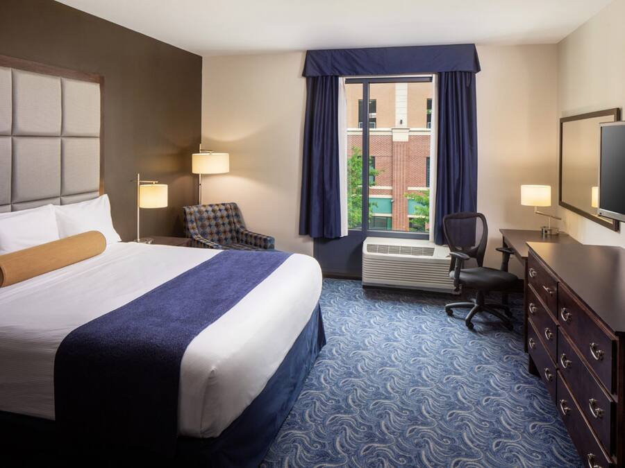 A hotel room with a large bed, a desk with a chair, a television, and a window with curtains.