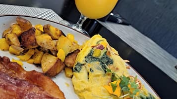 Une assiette de petit-déjeuner comprenant des œufs, des pommes de terre et du bacon, accompagnée d’un verre de jus d’orange.