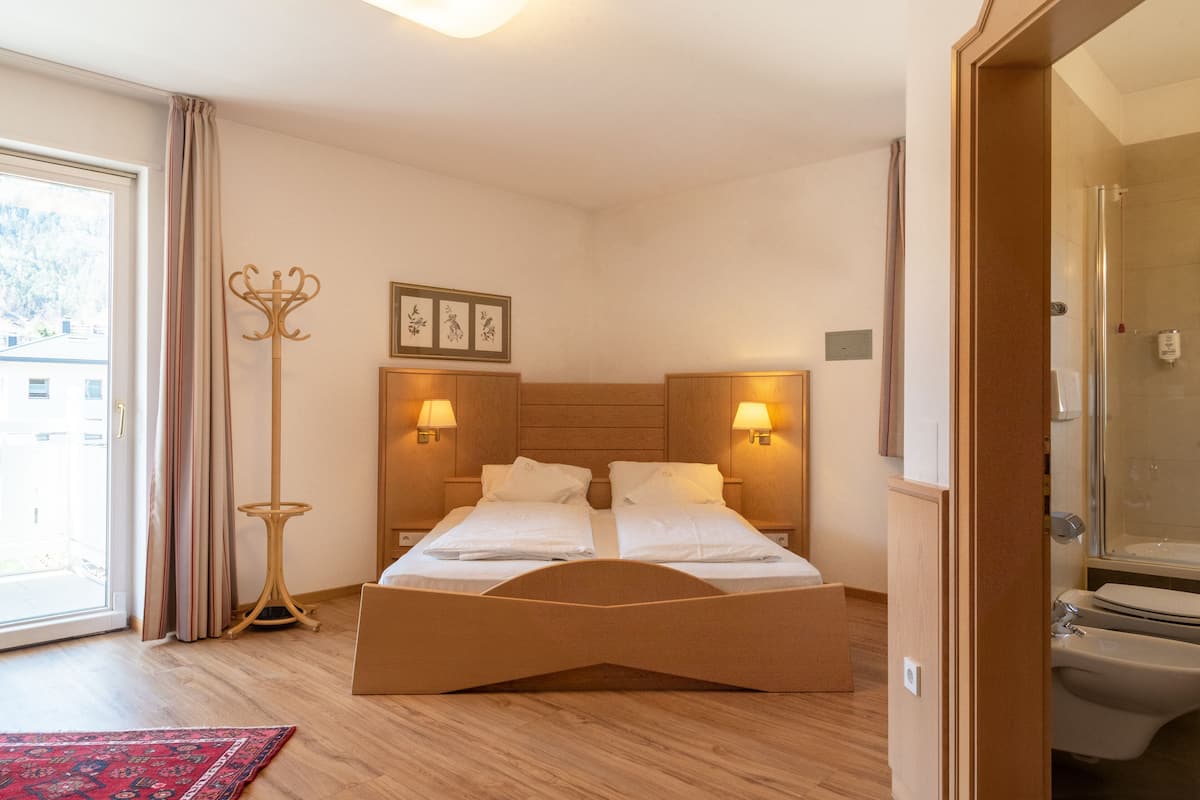 A bedroom with a wooden bed, two bedside lamps, a floor lamp, and a view of the outside through a sliding door.