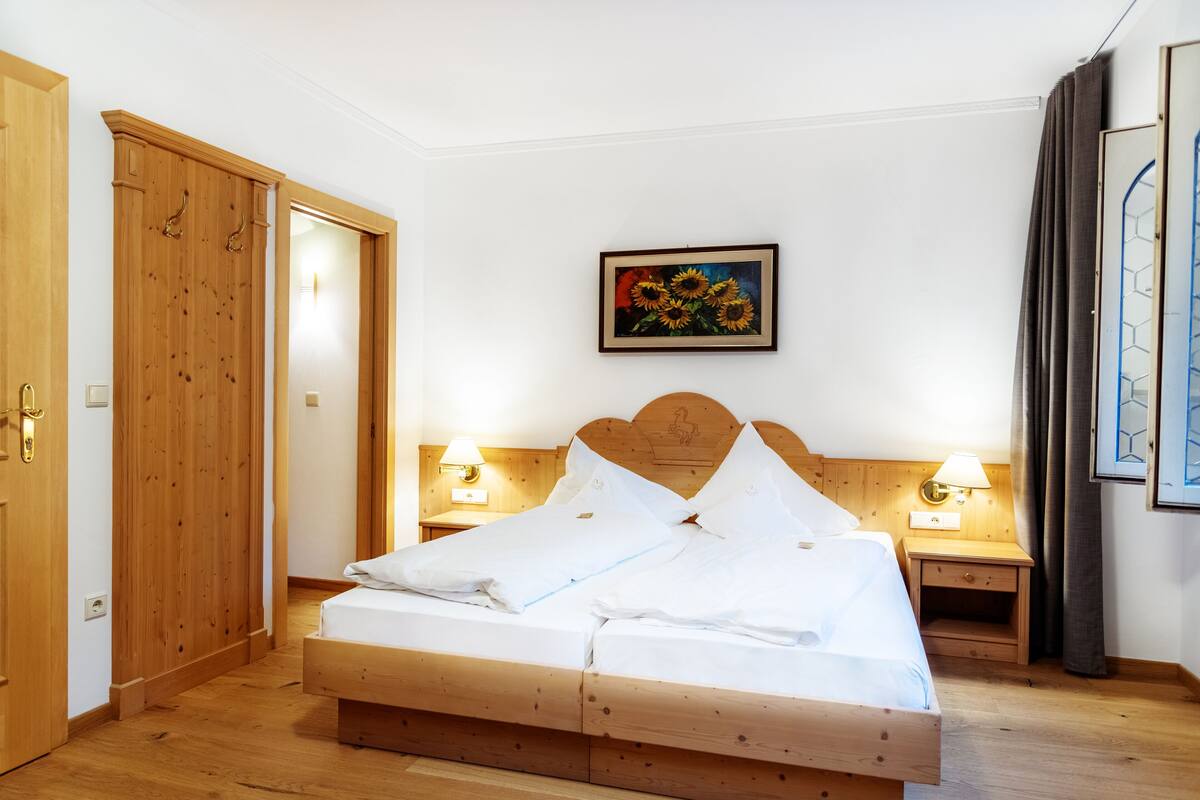 A wooden bed in a room with a wooden wardrobe and a painting of sunflowers on the wall.