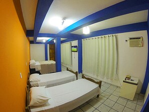A hotel room with two single beds, a television, a small heater, and a window with curtains.