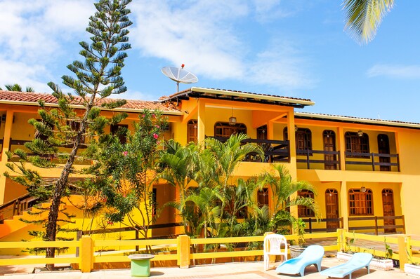 A two-story yellow building with a red-tiled roof, multiple balconies, and a satellite dish.