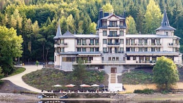A large, multi-story hotel with a prominent tower, situated by a lake with outdoor seating and a boat dock.