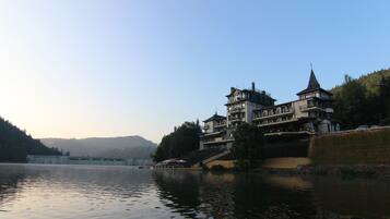 A large, multi-story building with a prominent tower, situated by a calm river.