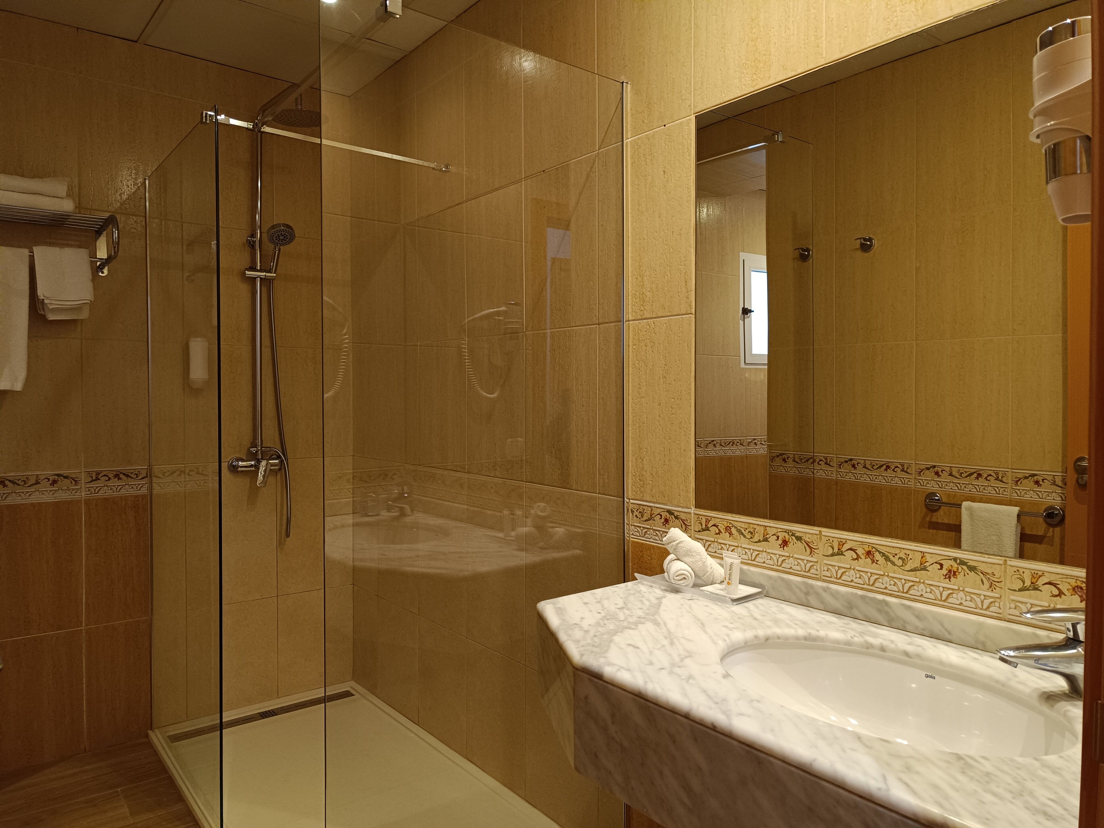 Un baño moderno con ducha envuelta en vidrio, lavamanos de mármol y un espejo grande.