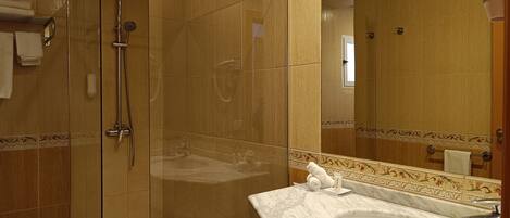 Un baño moderno con ducha envuelta en vidrio, lavamanos de mármol y un espejo grande.