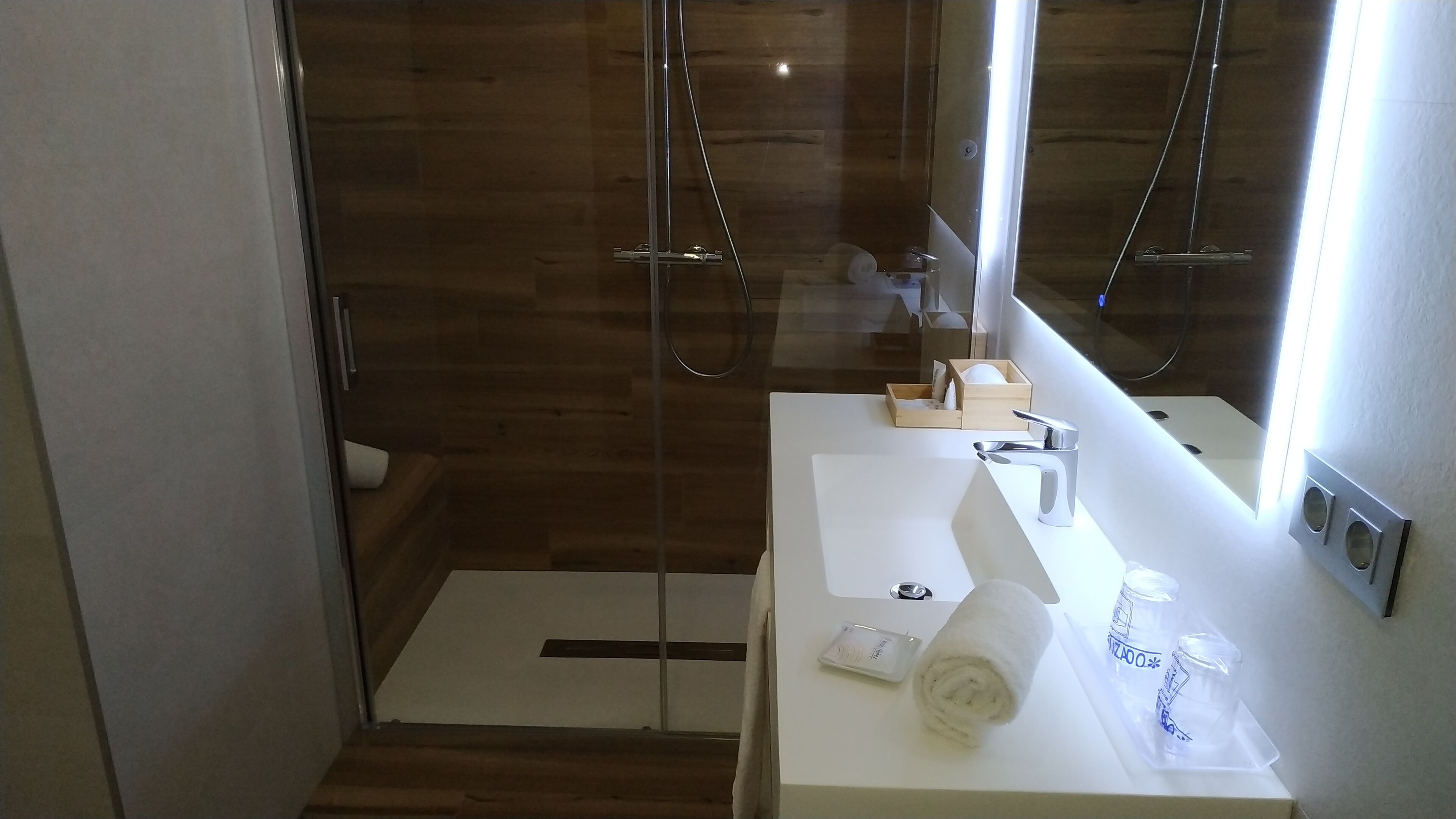 A modern bathroom with a wooden shower enclosure, a white sink with a mirror, and a towel on the counter.