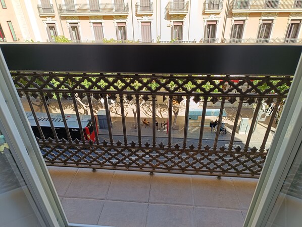 A balcony with a metal lattice railing, a tiled floor, and a view of a street with buildings and parked vehicles. - Méndez Núñez Alicante (Alicante)