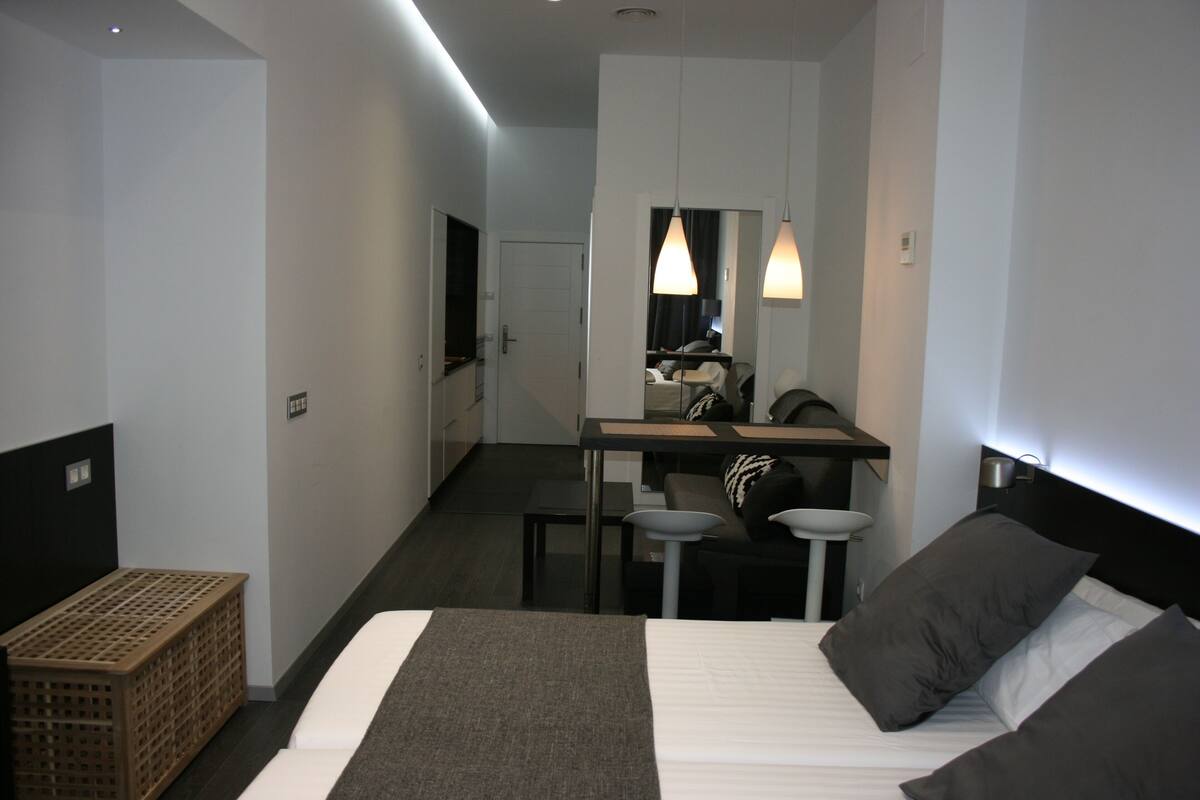 Une chambre d’hôtel moderne avec un grand lit, un bureau et un miroir. On y trouve une petite table et une chaise dans un coin.