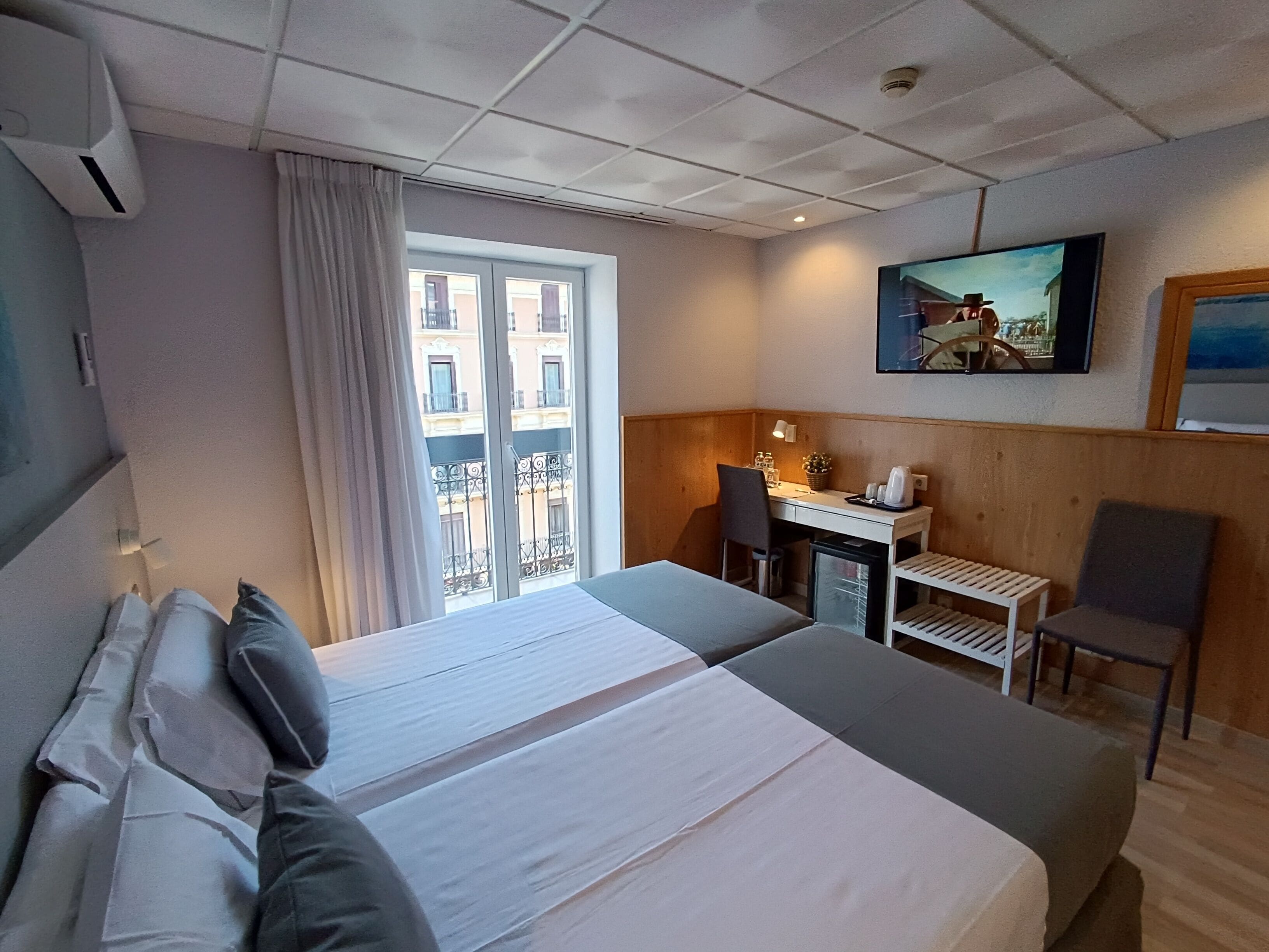 Een hotelkamer met een bed, een bureau, een stoel en een televisie aan de muur.