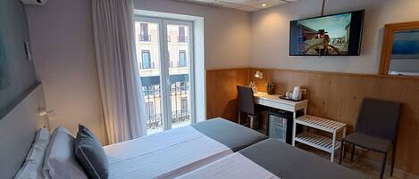 A hotel room with a bed, a desk, a chair, and a TV on the wall.