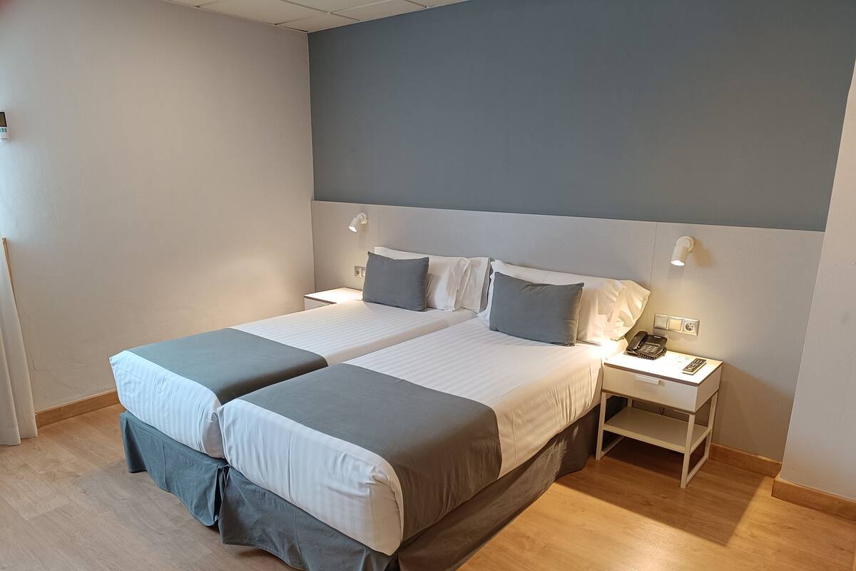 Un lit double avec une literie aux tons de gris et de blanc, des tables de chevet avec des lampes et un plancher en bois.