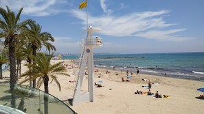 Een strand met palmbomen, een redershut en een stadsachtergrond.
