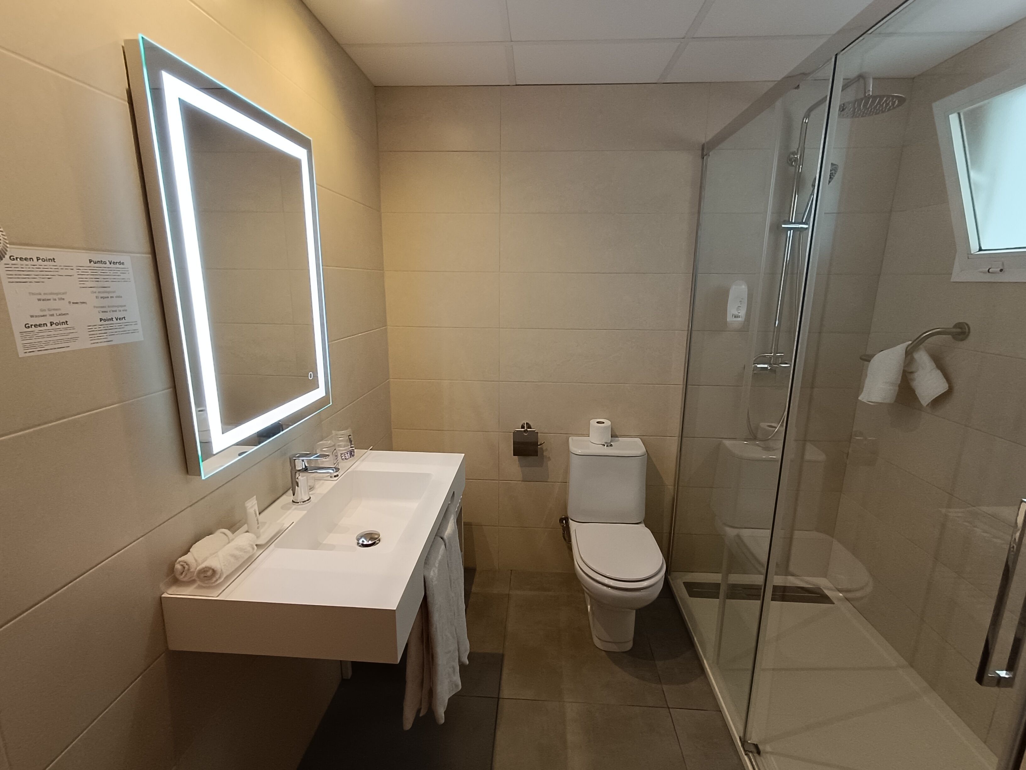 A modern bathroom with a large mirror, a sink, a toilet, and a glass-enclosed shower.