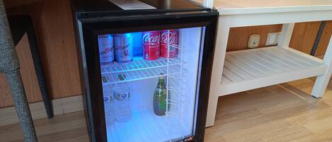 A small black refrigerator with a glass door, containing beverages and a bottle of water.