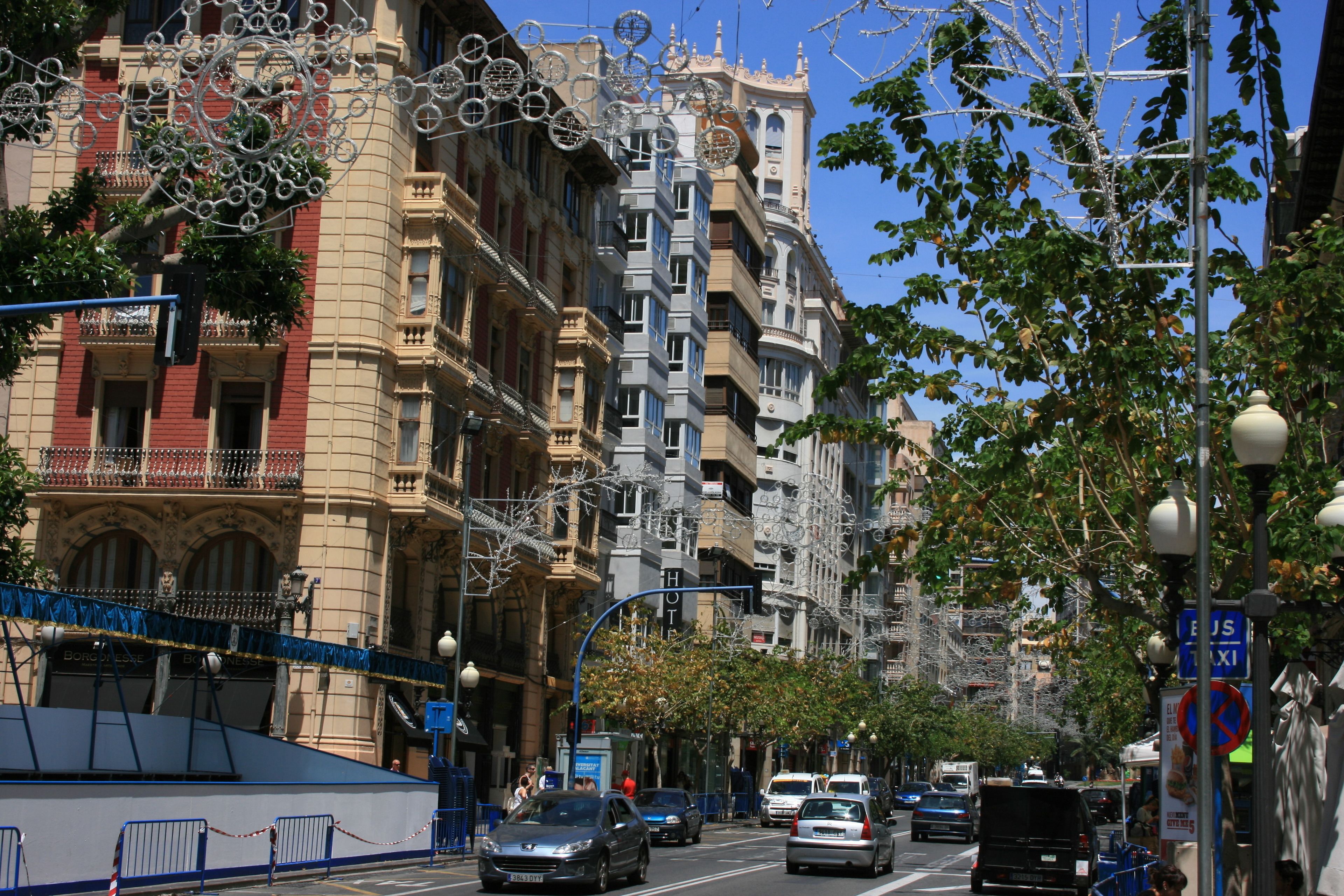 A street view with a hotel building featuring multiple balconies and a mix of architectural styles.