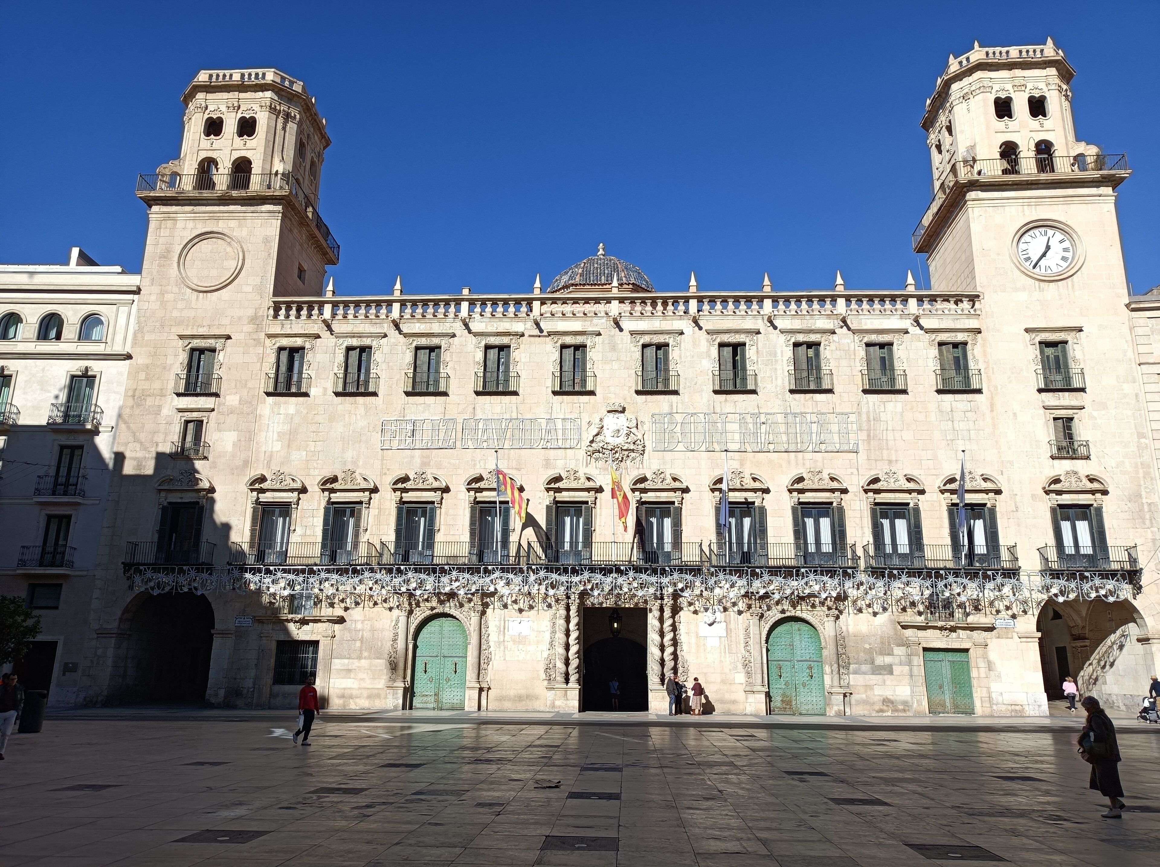 A historic building with a central dome, two clock towers, and a large open plaza.