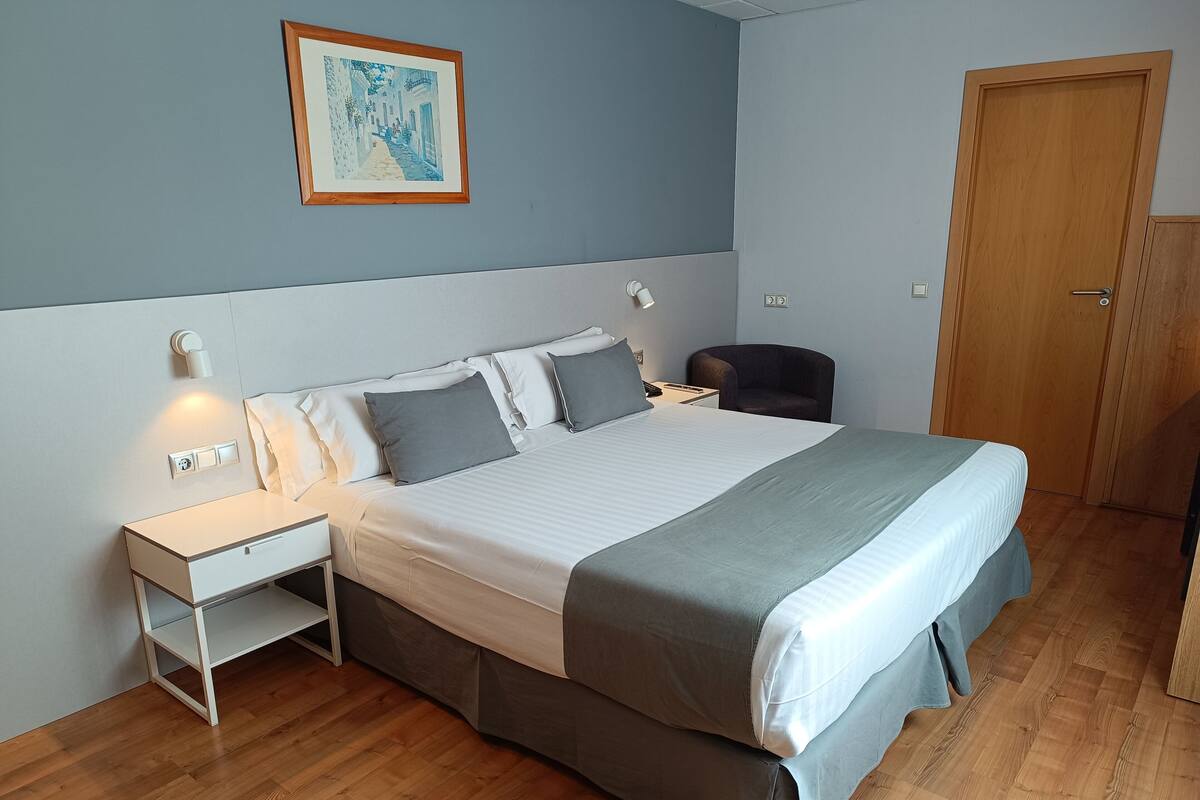 Une chambre bien rangée, avec un lit, des tables de chevet, une chaise et une porte.