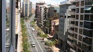 A city street lined with multi-story buildings, some with balconies and others with ground-level shops.