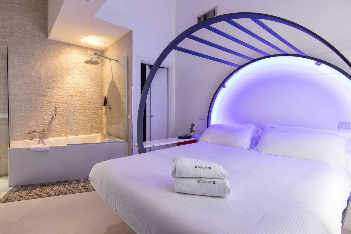 Habitación de hotel moderna con una cama grande, zona de ducha separada y un diseño de techo único.