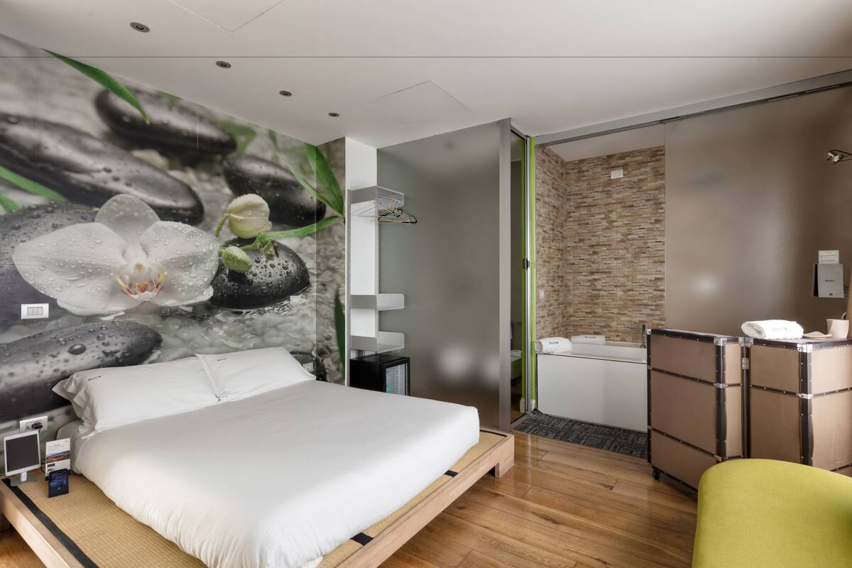 Una habitación de hotel moderna con una cama, zona de ducha y un mural en la pared.