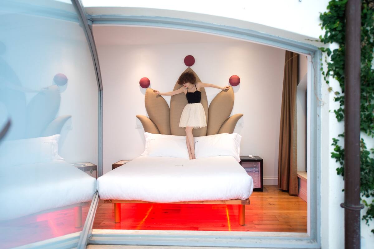 Una cama con un diseño de cabecera original, una mesita de noche y vistas al exterior.