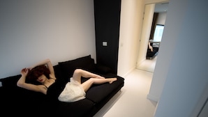 A person lying on a black sofa in a room with white walls and a visible door leading to another room. - WRooms Colosseum (Rome)