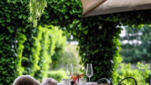An outdoor dining area with a table set for two, surrounded by lush greenery and a pergola. - Hotel Ter Zuidhoek (Roeselare)