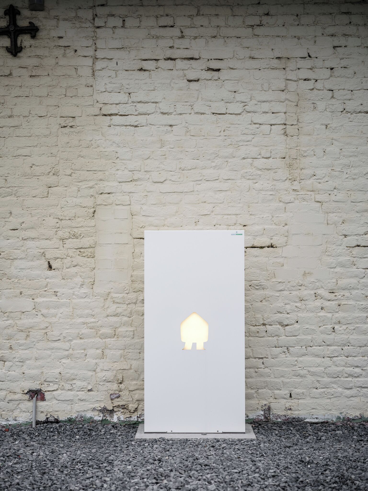 Un cartello bianco rettangolare con una semplice silhouette di una casa su un muro di mattoni bianchi.