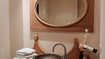A bathroom with a wooden vanity, a round mirror, a black sink, and a towel stack.