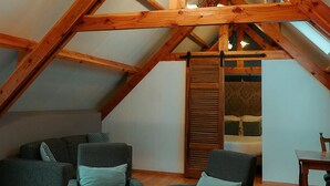 A loft-style room with exposed wooden beams, a ceiling fan, and a view of a bedroom through a wooden door. - Hotel Ter Zuidhoek (Roeselare)